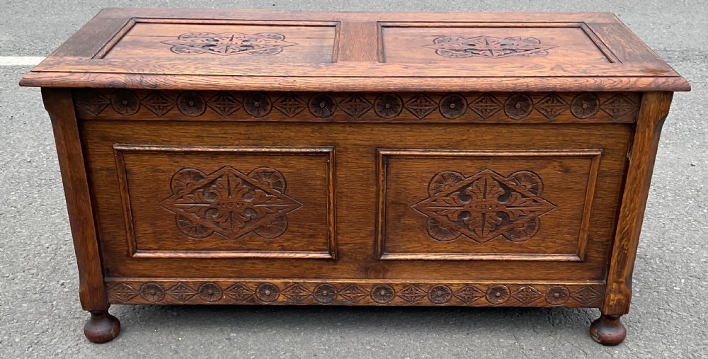 A dark carved oak blanket chest featuring panelled geometric relief detailing and turned front feet.