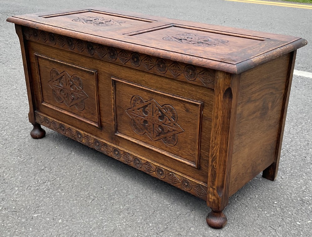 A dark carved oak blanket chest featuring panelled geometric relief detailing and turned front feet. View II