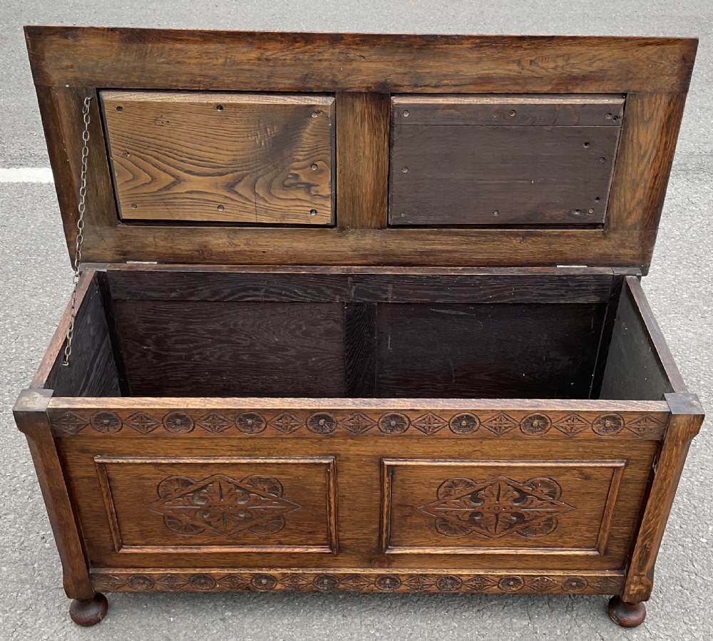 A dark carved oak blanket chest featuring panelled geometric relief detailing and turned front feet. View IV