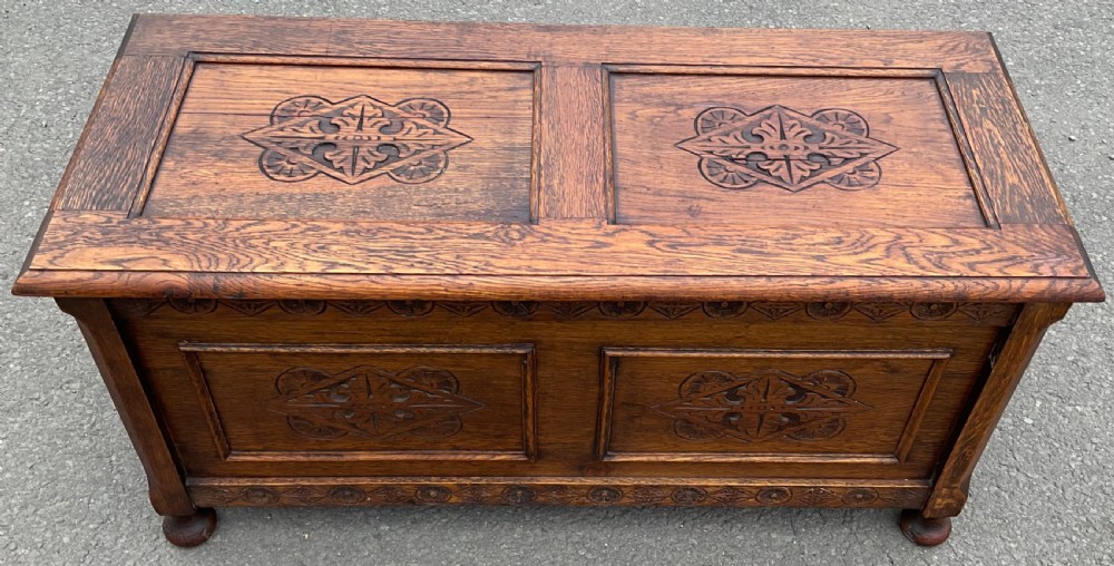 A dark carved oak blanket chest featuring panelled geometric relief detailing and turned front feet. View VI