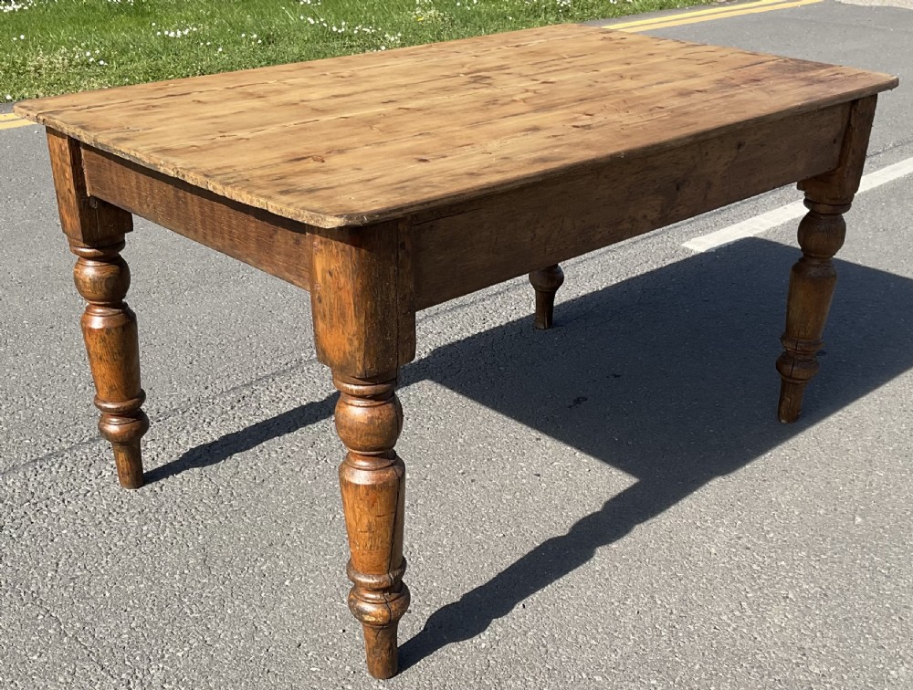 A rectangular Victorian pine kitchen table featuring a planked wood top and four turned wooden legs.