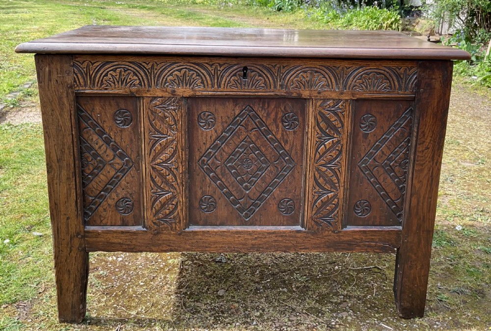 A dark oak coffer featuring three carved front panels with geometric lozenge motifs, an arched frieze, and a hinged top lid.