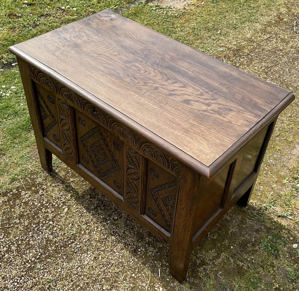 A dark oak coffer featuring three carved front panels with geometric lozenge motifs, an arched frieze, and a hinged top lid. View II