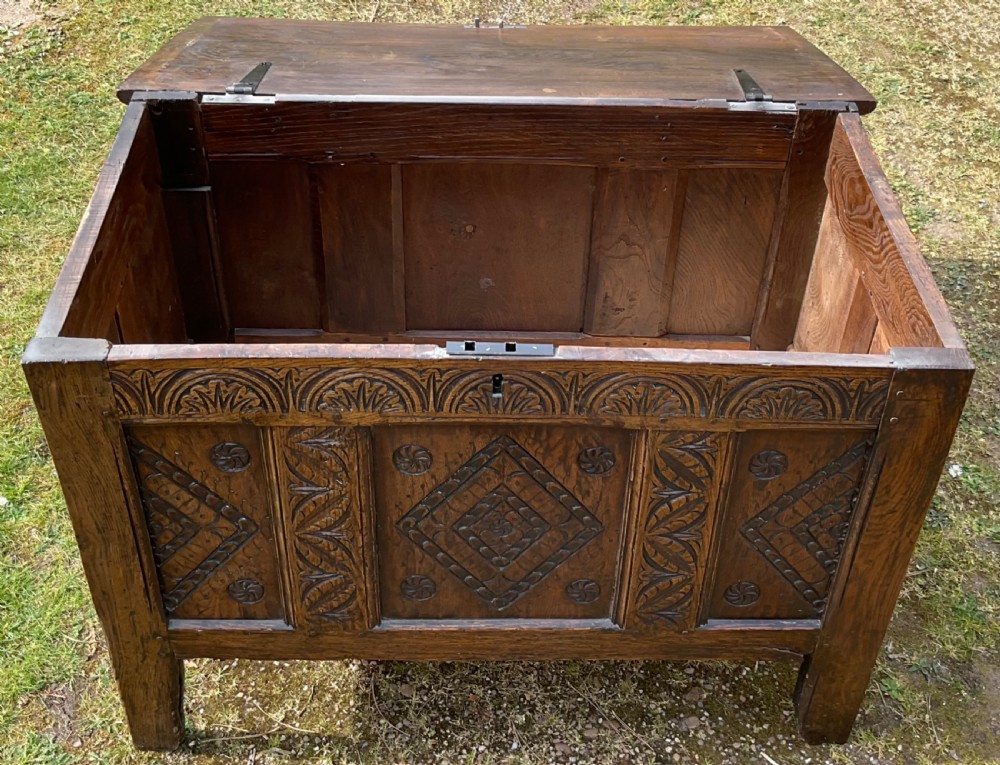 A dark oak coffer featuring three carved front panels with geometric lozenge motifs, an arched frieze, and a hinged top lid. View IV