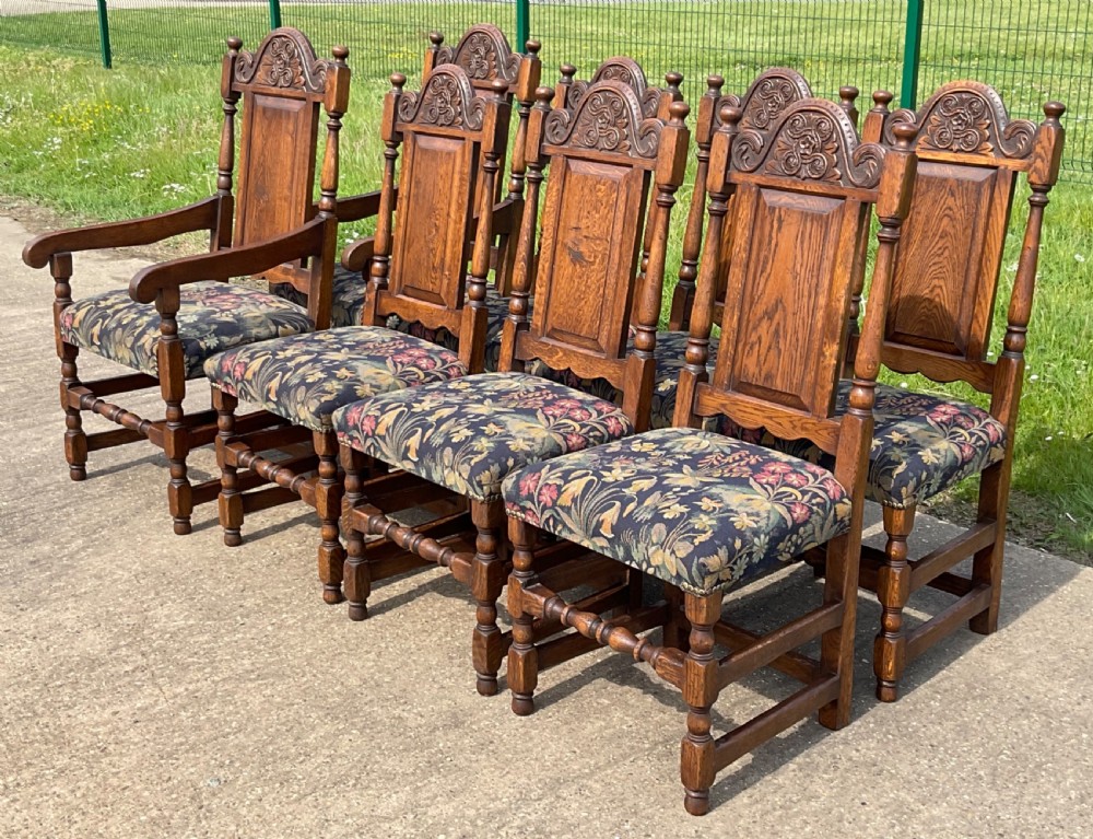 A set of eight Jacobean style oak dining chairs featuring carved arch crest rails, solid panel backs, turned stretchers, and floral tapestry upholstered seats. View II