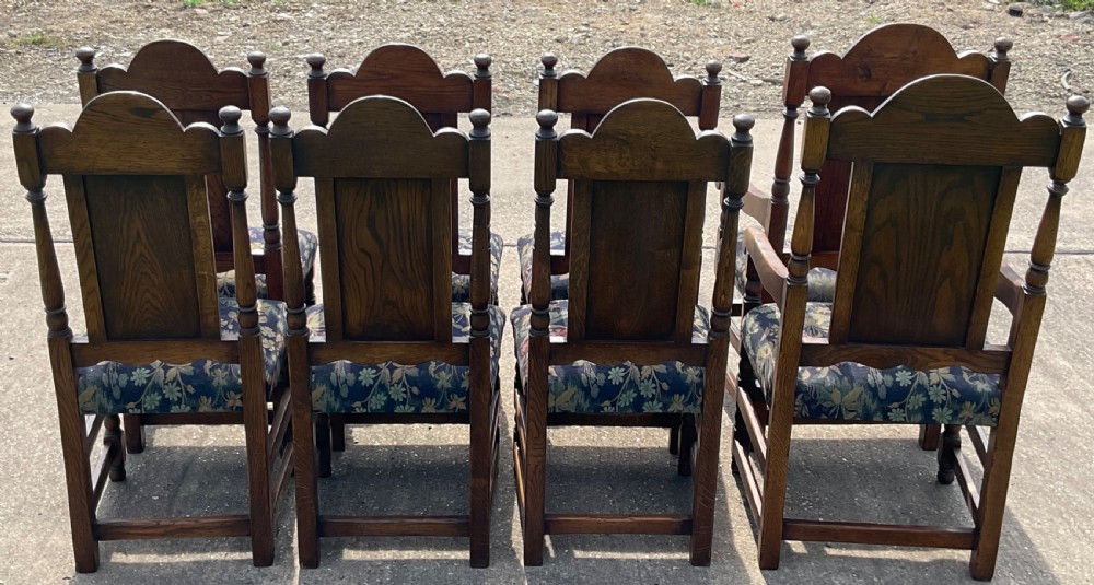 A set of eight Jacobean style oak dining chairs featuring carved arch crest rails, solid panel backs, turned stretchers, and floral tapestry upholstered seats. View V