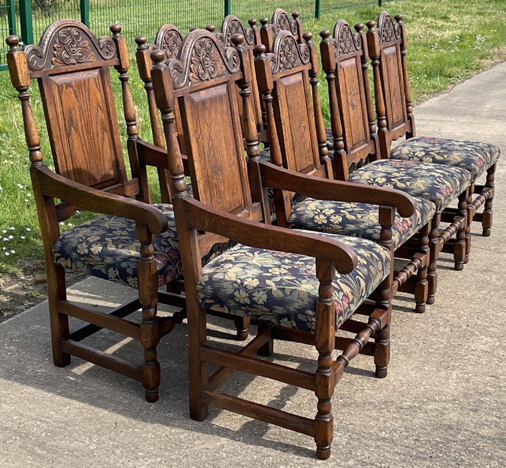 A set of eight Jacobean style oak dining chairs featuring carved arch crest rails, solid panel backs, turned stretchers, and floral tapestry upholstered seats. View VI