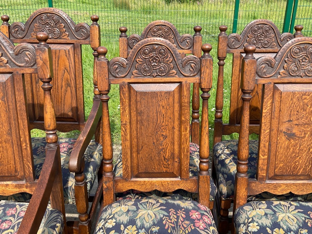 A set of eight Jacobean style oak dining chairs featuring carved arch crest rails, solid panel backs, turned stretchers, and floral tapestry upholstered seats. View VII