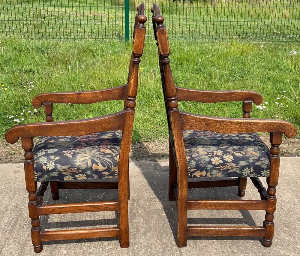 A set of eight Jacobean style oak dining chairs featuring carved arch crest rails, solid panel backs, turned stretchers, and floral tapestry upholstered seats. View VIII