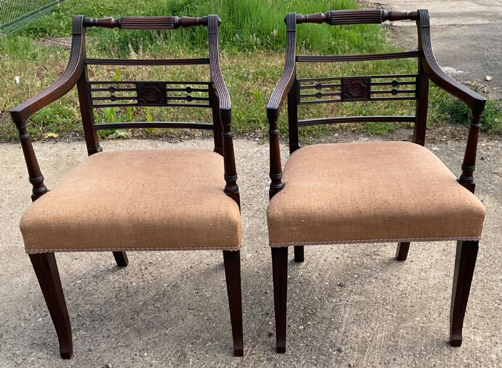 A pair of antique Georgian mahogany carver armchairs with reeded front legs, carved horizontal back splats, and neutral fabric seats.