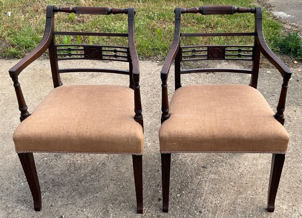 A pair of antique Georgian mahogany carver armchairs with reeded front legs, carved horizontal back splats, and neutral fabric seats. View II