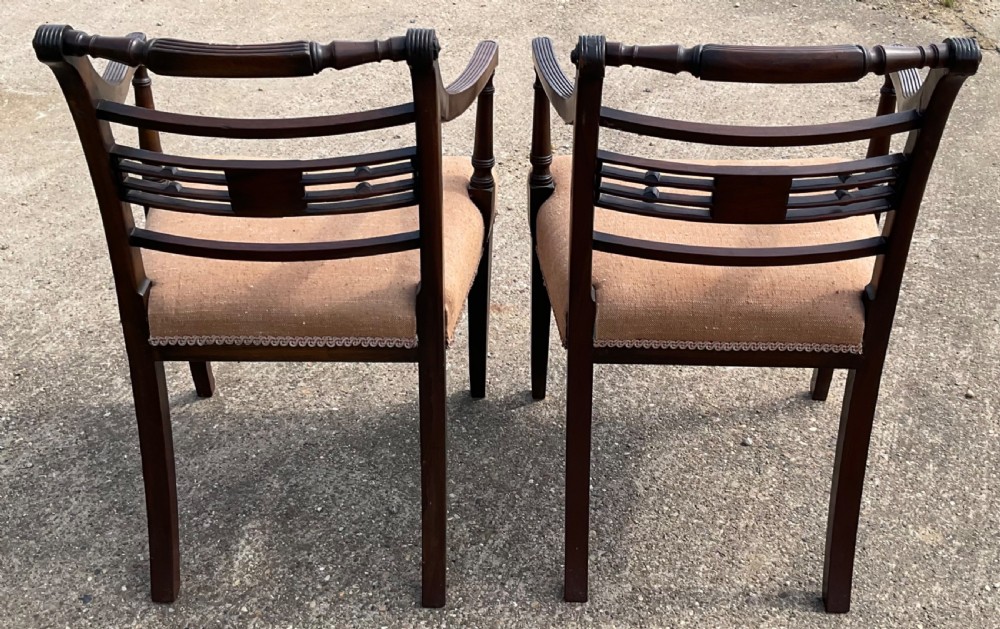 A pair of antique Georgian mahogany carver armchairs with reeded front legs, carved horizontal back splats, and neutral fabric seats. View X