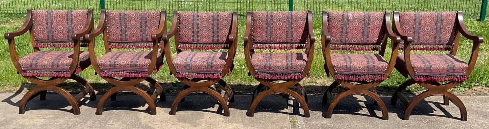 A set of six oak armchairs featuring cross-frame legs, curved armrests, red patterned geometric fabric, and fringed seat aprons.