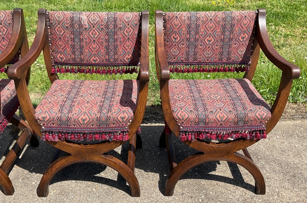 A set of six oak armchairs featuring cross-frame legs, curved armrests, red patterned geometric fabric, and fringed seat aprons. View II