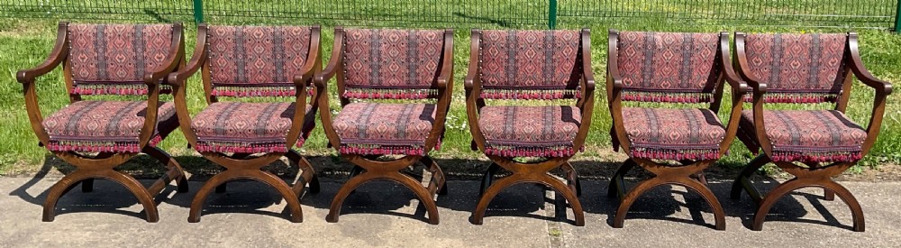 A set of six oak armchairs featuring cross-frame legs, curved armrests, red patterned geometric fabric, and fringed seat aprons. View III