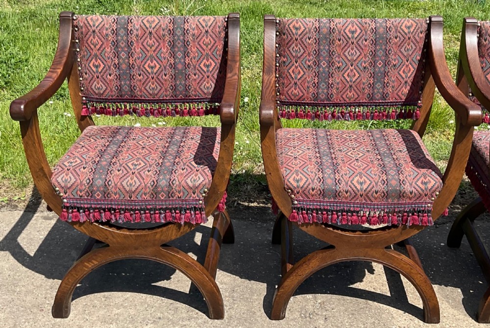 A set of six oak armchairs featuring cross-frame legs, curved armrests, red patterned geometric fabric, and fringed seat aprons. View IV