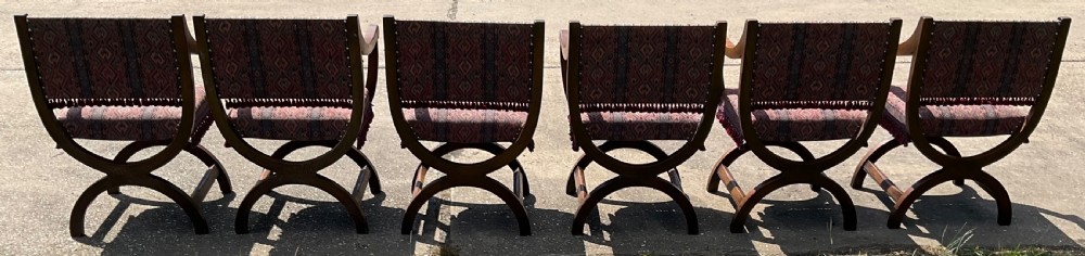 A set of six oak armchairs featuring cross-frame legs, curved armrests, red patterned geometric fabric, and fringed seat aprons. View VIII