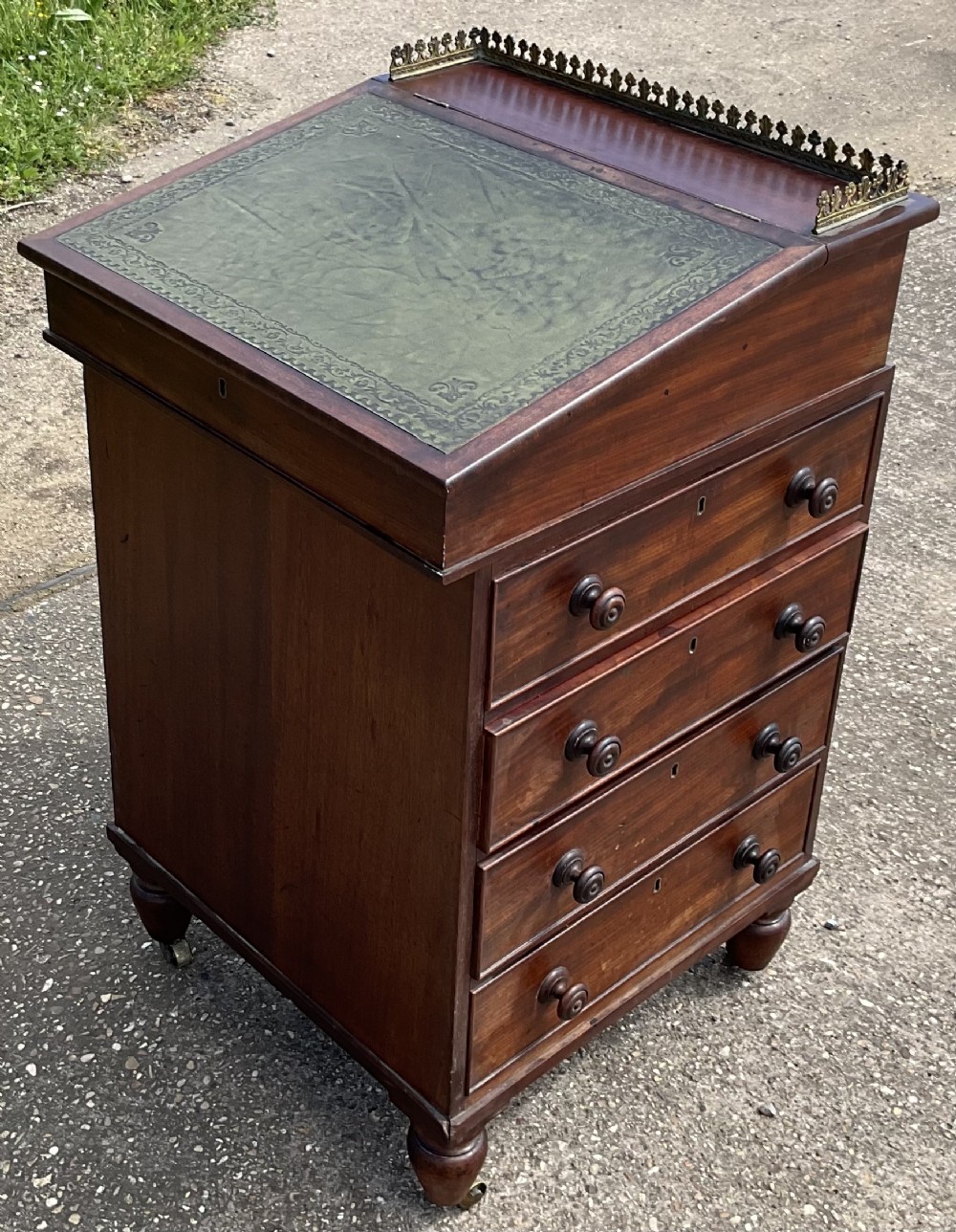 A Regency mahogany davenport desk featuring a green leather sloped writing surface, brass gallery rail, and side drawers with turned handles on castors.