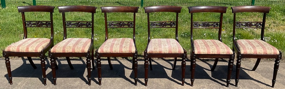 A set of six dark rosewood Regency dining chairs featuring carved bar back rails, turned front legs, and striped upholstered seats.