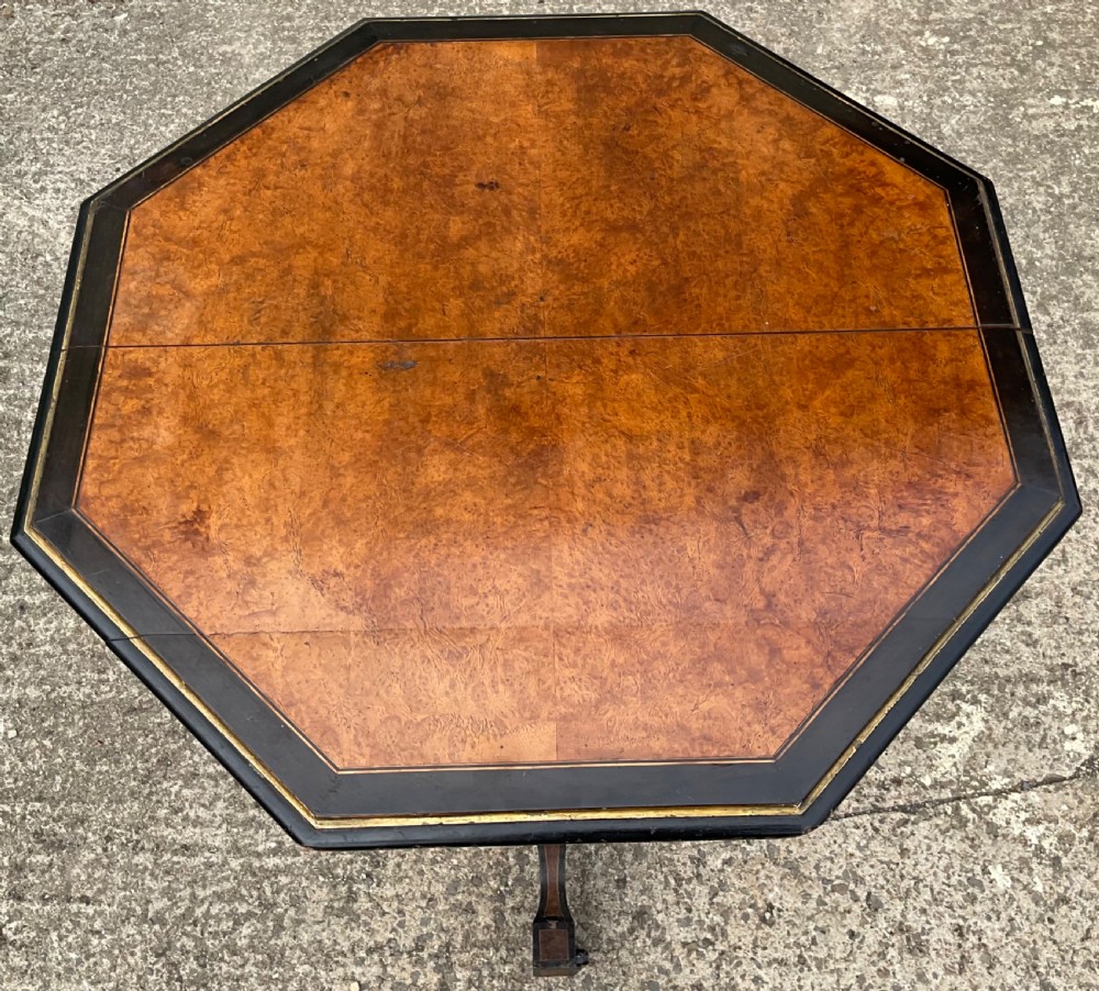 An octagonal antique centre table featuring a burr walnut veneered top, ebonised borders with gilt detailing, and a central turned pedestal supported by four splayed legs. View III
