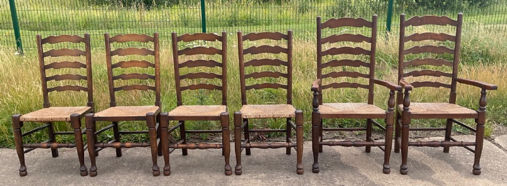 A set of six warm brown wood ladderback dining chairs with hand-woven rush seats, comprising four side chairs and two carver armchairs.