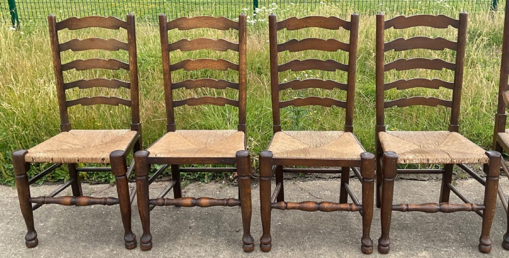 A set of six warm brown wood ladderback dining chairs with hand-woven rush seats, comprising four side chairs and two carver armchairs. View V