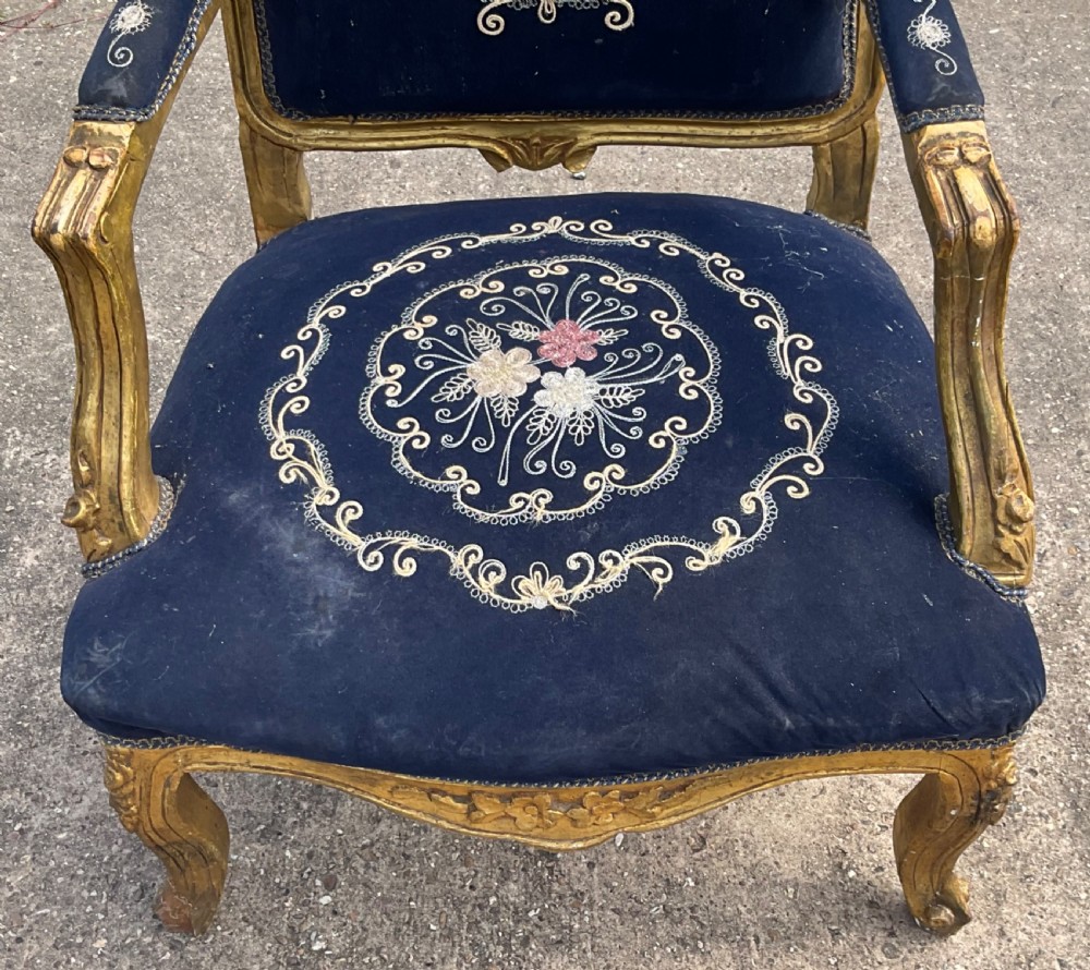 A Victorian giltwood armchair featuring a gold carved frame, cabriole legs, padded armrests, and dark blue velvet upholstery decorated with central floral embroidery. View VI