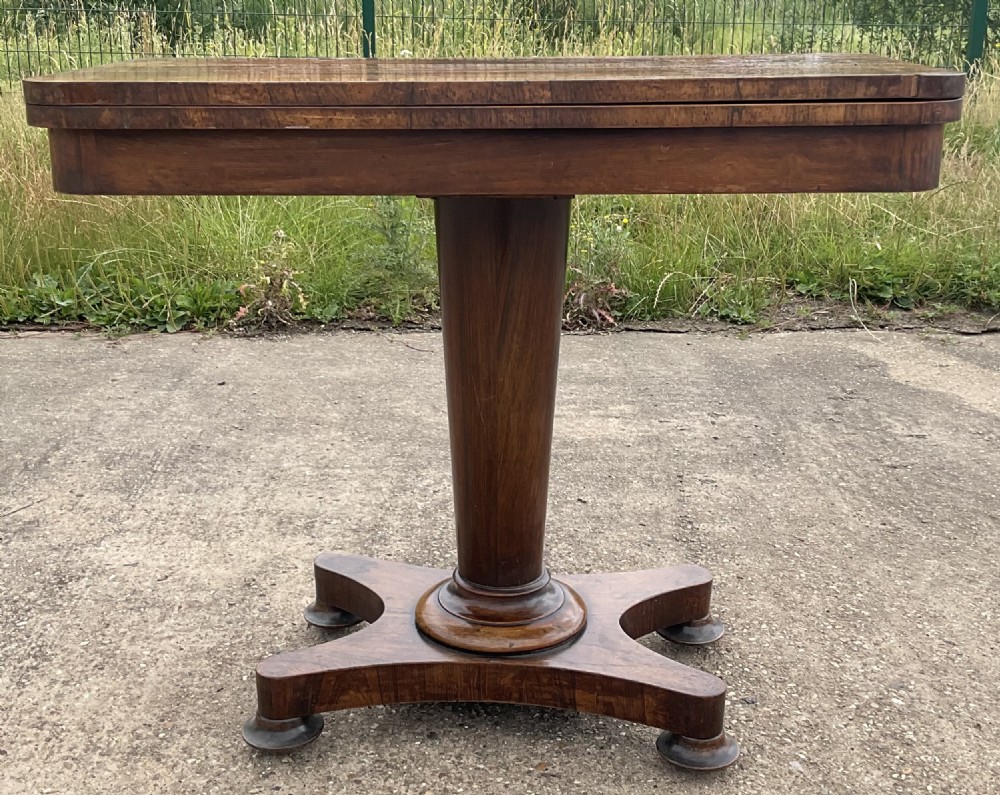 An early Victorian mahogany foldover card table featuring a figured wood top on a tapered central pedestal with a quadform base. View II