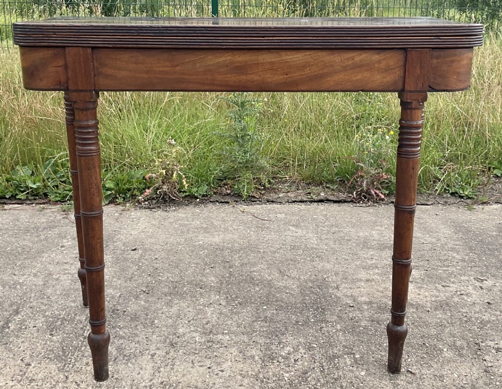 A Georgian mahogany foldover tea table with ring-turned legs and a reeded edge on a flat concrete surface.