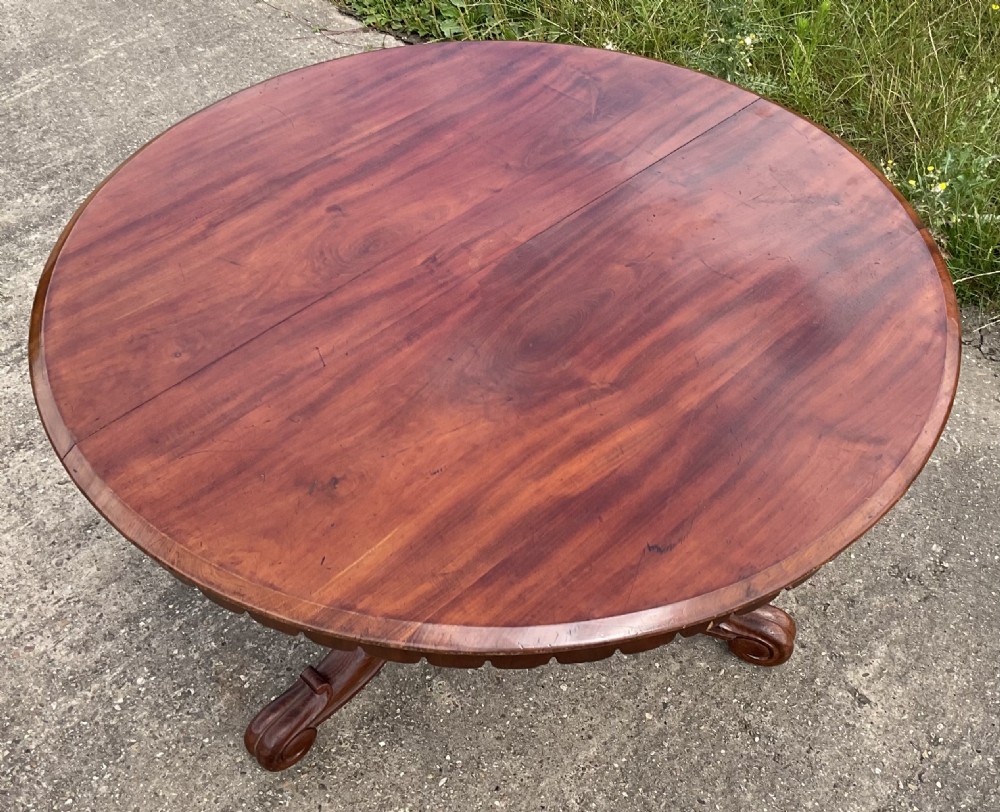 A Victorian circular mahogany centre table with a polished flame mahogany top and carved scrolled feet.