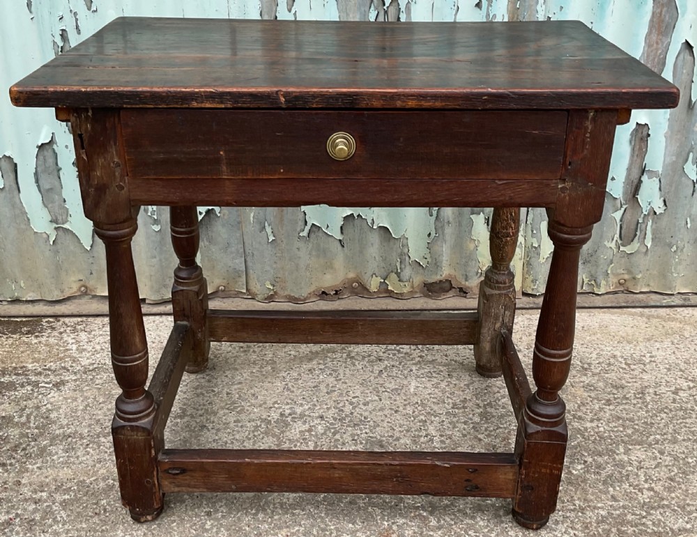A dark brown antique oak side table featuring a single drawer with a brass knob, turned legs, and a four-piece stretcher base.