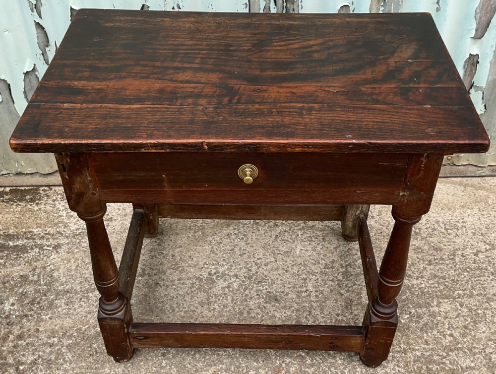 A dark brown antique oak side table featuring a single drawer with a brass knob, turned legs, and a four-piece stretcher base. View II