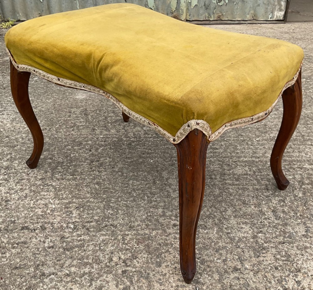 A Victorian low stool featuring a concave olive velvet upholstered seat, trim detail, and four dark carved walnut cabriole legs. View IV