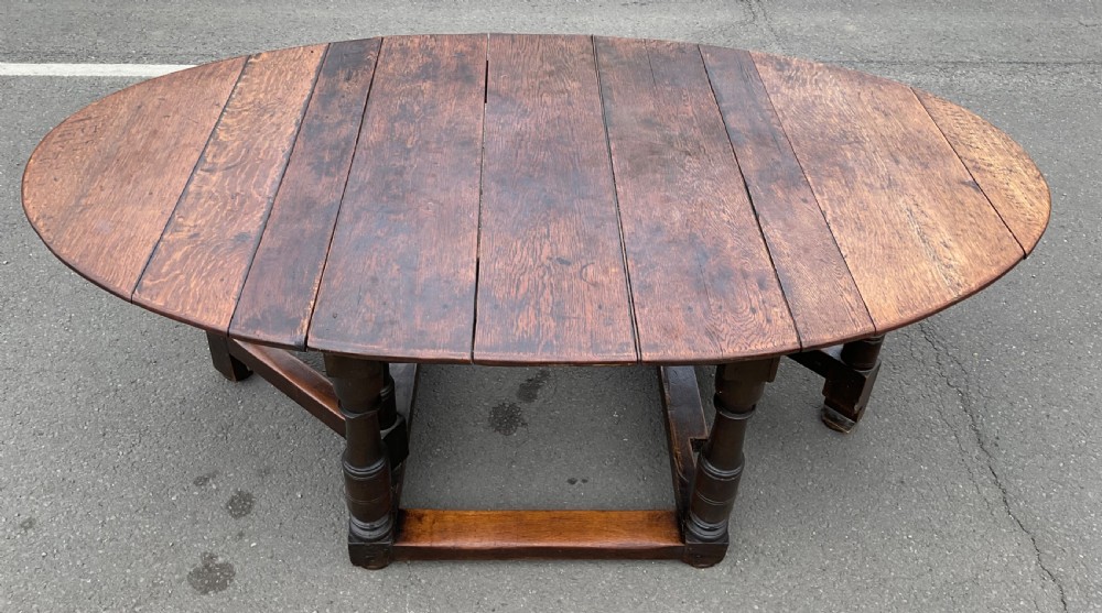 A large antique oak gateleg dining table featuring an oval top with drop leaves, supported by turned legs and stretcher rails. View II