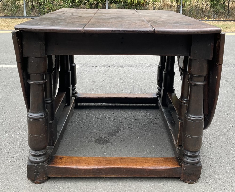 A large antique oak gateleg dining table featuring an oval top with drop leaves, supported by turned legs and stretcher rails. View V