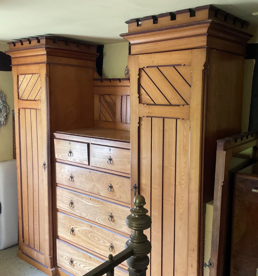 A large Aesthetic Movement pitch pine triple wardrobe featuring a central chest of drawers flanked by two tall cupboard doors with diagonal panel detailing and a castellated top cornice. View IV