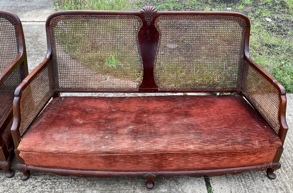 A three-piece antique mahogany lounge suite consisting of a two-seater settee and two matching armchairs with cane side panels, carved central splats, and worn red velvet cushions. View II