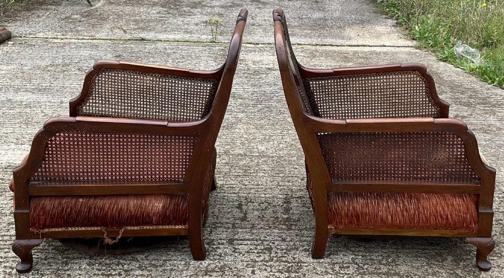 A three-piece antique mahogany lounge suite consisting of a two-seater settee and two matching armchairs with cane side panels, carved central splats, and worn red velvet cushions. View IV