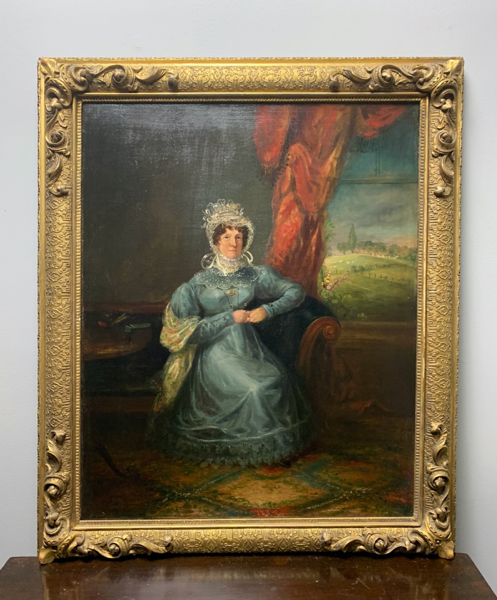 An antique oil portrait depicting a seated lady in a blue gown and lace bonnet, set within an ornate gilded frame.