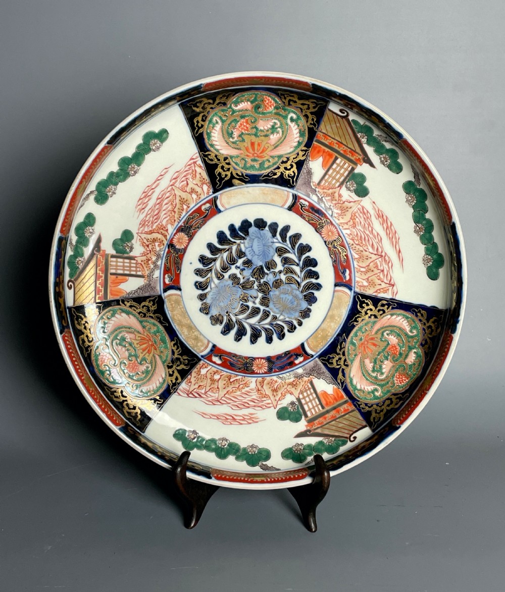 A large circular Japanese Imari porcelain shallow bowl featuring detailed panelled motifs in cobalt blue, iron-red, green, and gold hand-painted enamel.