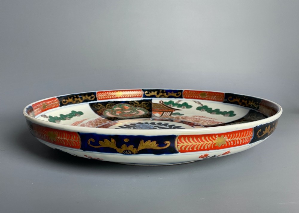 A large circular Japanese Imari porcelain shallow bowl featuring detailed panelled motifs in cobalt blue, iron-red, green, and gold hand-painted enamel. View VII
