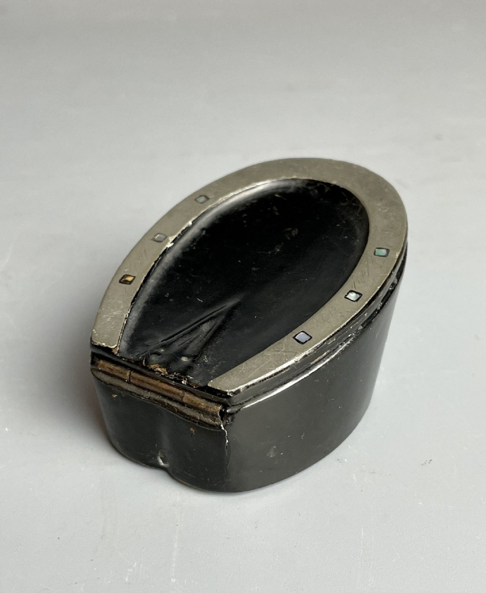 A Victorian black japanned papier-mache snuff box shaped like a horses hoof with a metal horseshoe rim featuring mother-of-pearl inlays.