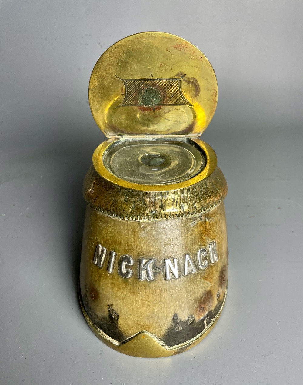 A Victorian horse hoof inkwell featuring brass mounts, a hinged brass lid, and silver lettering reading NICK-NACK. View III