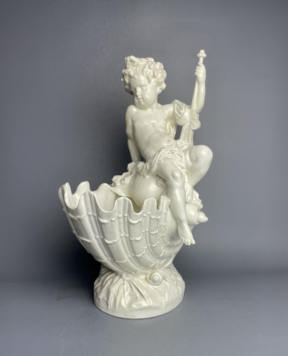 A white glazed ceramic centrepiece featuring a cherub figure seated on a shell atop a naturalistic base.