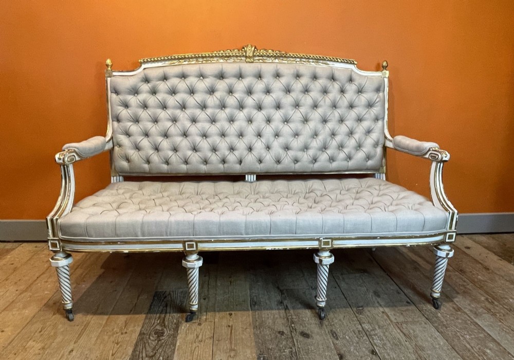 An antique Louis XVI style painted and gilt sofa with button-tufted grey upholstery and spiral fluted legs.