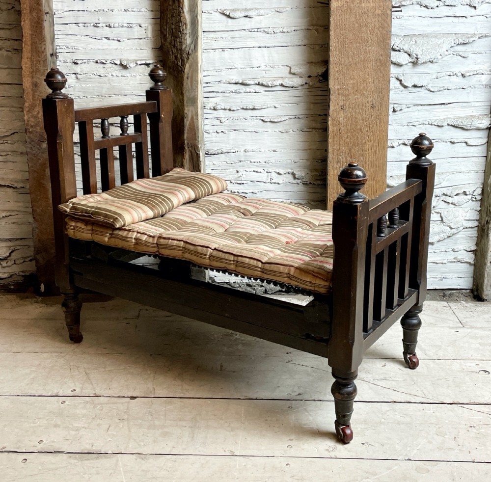 A dark wood Edwardian miniature bed with turned finials, castors, and a striped fabric mattress with matching pillow.