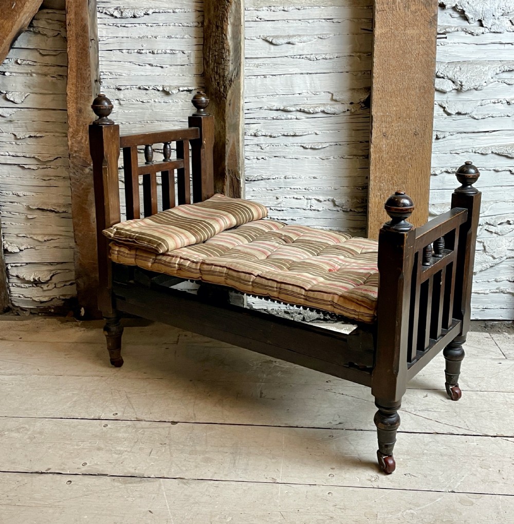 A dark wood Edwardian miniature bed with turned finials, castors, and a striped fabric mattress with matching pillow. View II