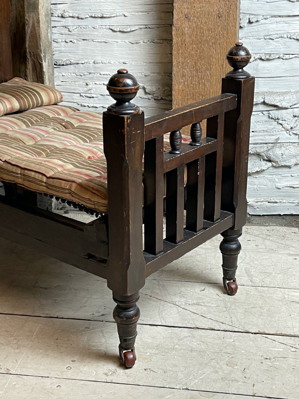 A dark wood Edwardian miniature bed with turned finials, castors, and a striped fabric mattress with matching pillow. View III