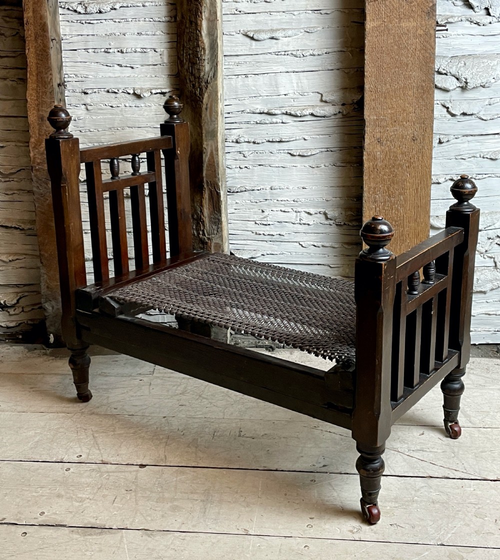A dark wood Edwardian miniature bed with turned finials, castors, and a striped fabric mattress with matching pillow. View IV