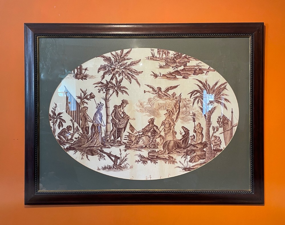 An oval copperplate-printed sepia textile fragment depicting an allegorical scene set inside a green mount and dark wooden frame.